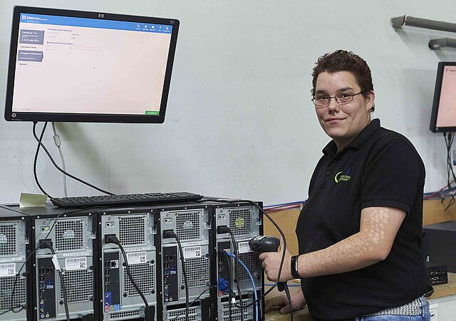 lächelnde AfB Mitarbeiterin in Testung mit fünf PC und einem Monitor
