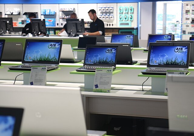 Mit neuem Betriebssystem eingespielte Laptops in Reihe aufgestellt / Technisches Datenblatt beiliegend / Verkaufsgespräch im Hintergrund